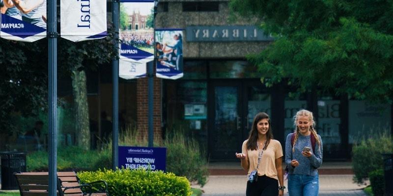 两个女大学生一起走在威尼斯人平台图书馆前的小路上